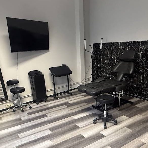 Tattoostudio Tattooraum mit Liege, Stühlen und TV auf Holzboden.