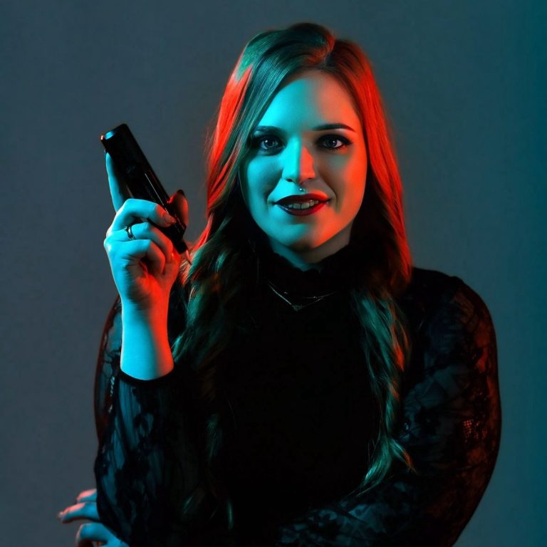 Alicia Funck - Alice Wonderline Tattoo Alicia Funck umgeben von blauen und roten Lichtern mit Tattoomaschine in der Hand.